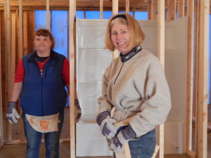 Two women standing in a room with construction materials.