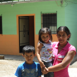 A woman and two children standing in front of a house.