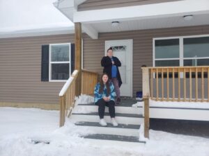 Two people standing on steps in front of a house.